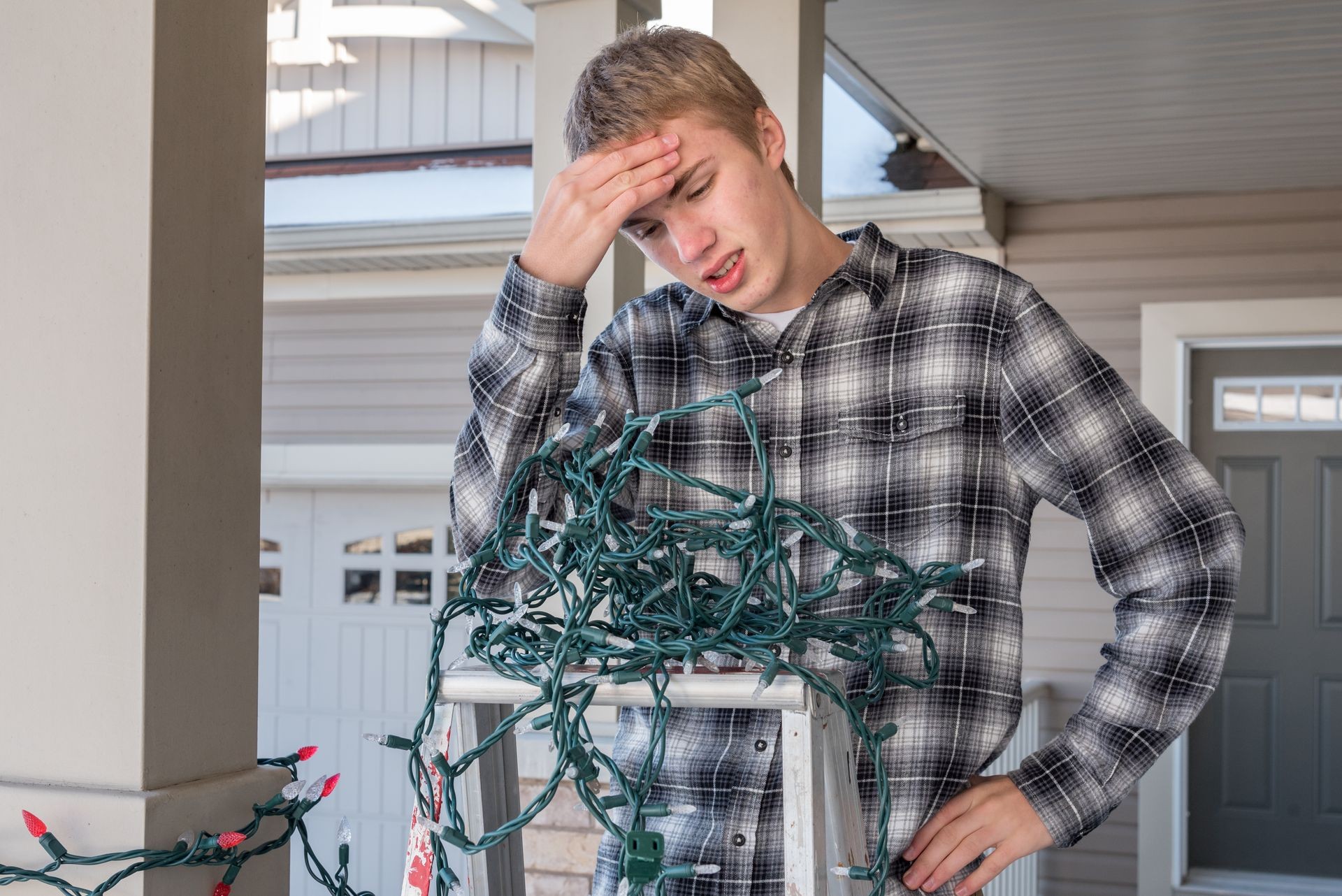 Man frustrated on a ladder while hanging tangled holiday lights.